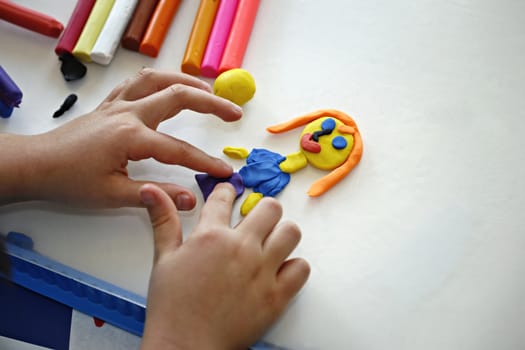 Hands of little girl making doll from colorful clay dough (plasticine