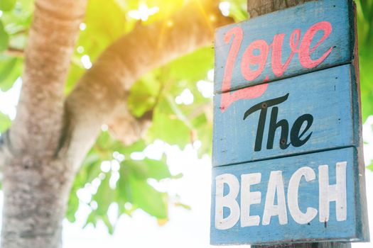 Love the beach word on wood board hang on tree beside summer beach background.