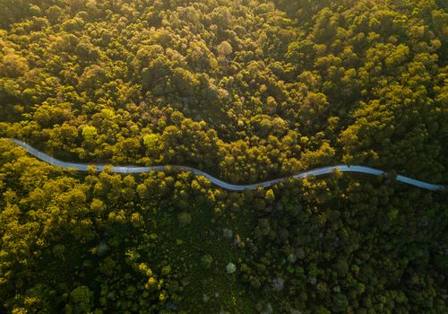 Top view ofcountryside road passing through the green forrest and mountain