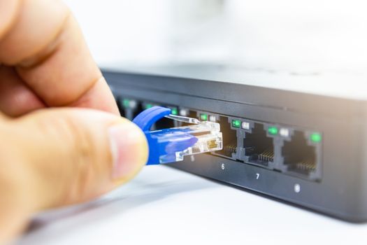 Hand of man holding The blue network cables connect port switch on white table concept internet network connection