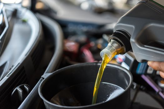 Car mechanic or serviceman fills a fresh lubricant engine oil at car garage for repair or maintenance a car