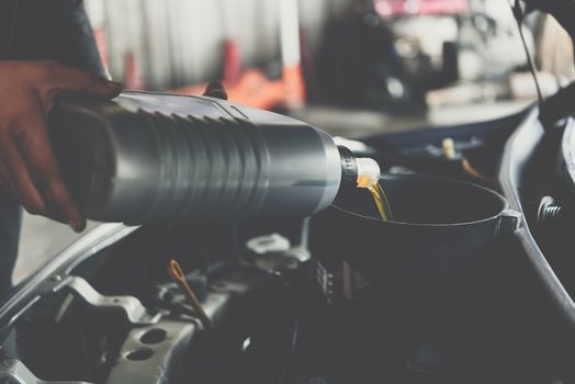 Car mechanic or serviceman fills a fresh lubricant engine oil at car garage for repair or maintenance a car