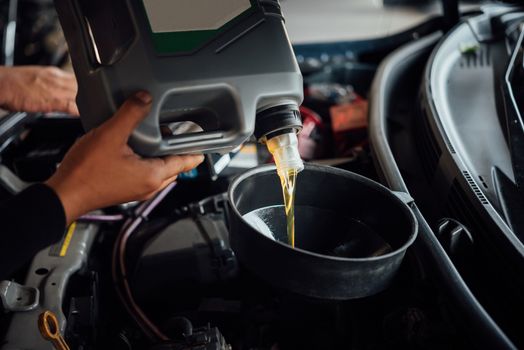 Car mechanic or serviceman fills a fresh lubricant engine oil at car garage for repair or maintenance a car