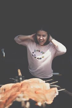 Asian woman chef cooking Barbecued Suckling Pig by roasting pork on charcoal for sale at Thai street food market or restaurant in Thailand