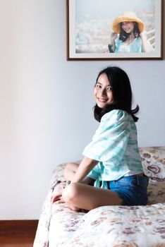 Asian pretty woman short jeans sitting on bed in bedroom alone with happiness and joyful emotion in concept cheerful feeling, pleasure, fun in life