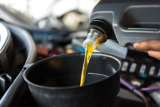 Car mechanic or serviceman fills a fresh lubricant engine oil at car garage for repair or maintenance a car