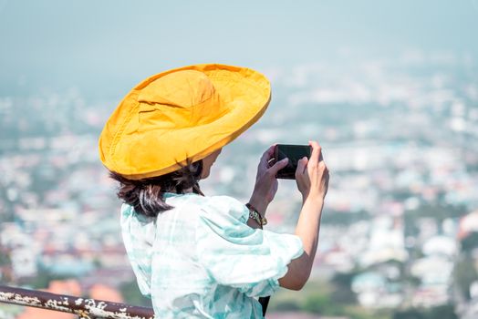 Asian pretty cute woman with hat relax and use smartphone at seaside city landscape viewpoint on mountain with happy and freedom emotion in concept travel, vacation, leisure in life