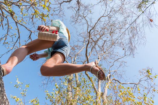 Low angle view of sexy woman short jeans midair by jumping, crossing step over camera shot below in forest with tree and sky overhead in concept travel, active lifestyle, overcome obstacles in life