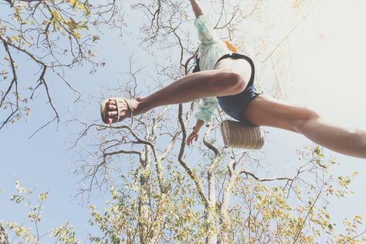 Low angle view of sexy woman short jeans midair by jumping, crossing step over camera shot below in forest with tree and sky overhead in concept travel, active lifestyle, overcome obstacles in life