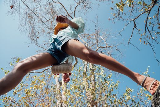 Low angle view of sexy woman short jeans midair by jumping, crossing step over camera shot below in forest with tree and sky overhead in concept travel, active lifestyle, overcome obstacles in life