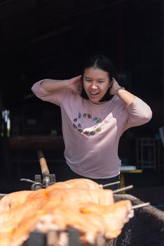 Asian woman chef cooking Barbecued Suckling Pig by roasting pork on charcoal for sale at Thai street food market or restaurant in Thailand