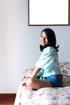 Asian pretty woman short jeans sitting on bed in bedroom alone with happiness and joyful emotion in concept cheerful feeling, pleasure, fun in life