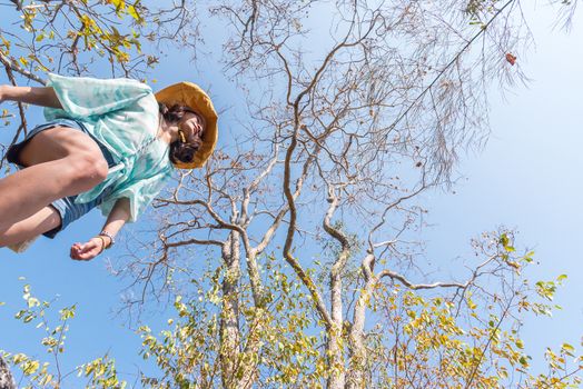 Low angle view of sexy woman short jeans midair by jumping, crossing step over camera shot below in forest with tree and sky overhead in concept travel, active lifestyle, overcome obstacles in life