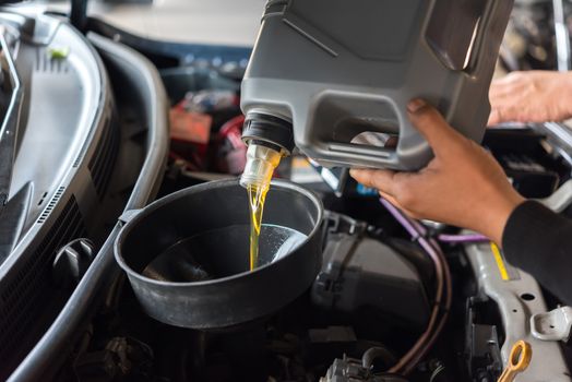 Car mechanic or serviceman fills a fresh lubricant engine oil at car garage for repair or maintenance a car