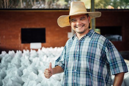 Asian man farmer agriculturist happy thumbs up at a Fertilizer composting plant with Organic Fertilizer, Compost (Aerobic Microorganisms) from animal waste for use in the organic agriculture industry