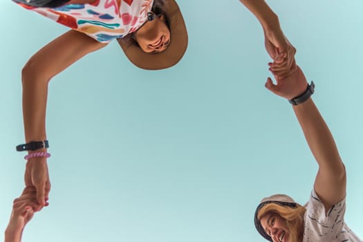 Low angle view of cute three asian women hold hands circle running round camera shot below with sky overhead in concept travel, happy and fun lifestyle, friendship. Pastel vintage style