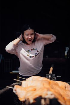 Asian woman chef cooking Barbecued Suckling Pig by roasting pork on charcoal for sale at Thai street food market or restaurant in Thailand