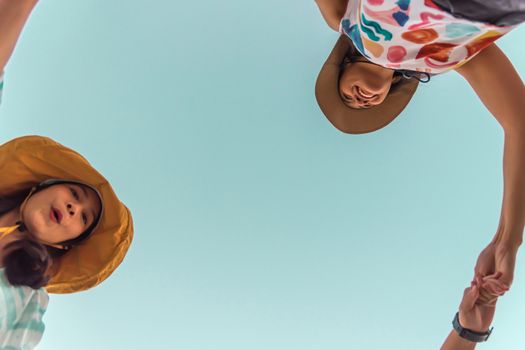 Low angle view of cute three asian women hold hands circle running round camera shot below with sky overhead in concept travel, happy and fun lifestyle, friendship. Pastel vintage style