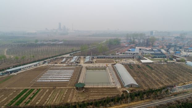 Small rural poor villages, surrounded by farm land, small factories and train tracks outside Beijing during extreme pollution gray day. China.
