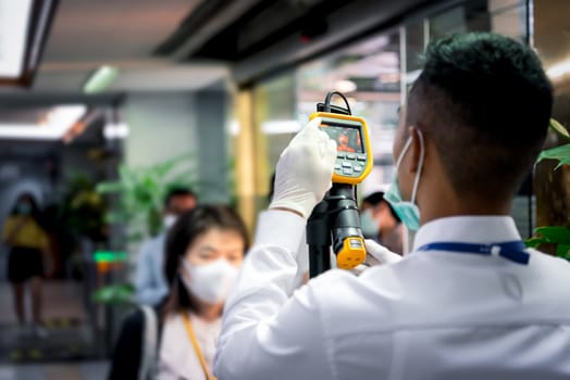 Asian people waiting for body temperature check before access to building for against epidemic flu covid19 or corona virus from wuhan in office by thermoscan or infrared thermal camera