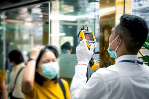 Asian people waiting for body temperature check before access to building for against epidemic flu covid19 or corona virus from wuhan in office by thermoscan or infrared thermal camera