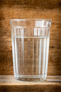 One glass of water, illuminated with natural light, on a wooden plank