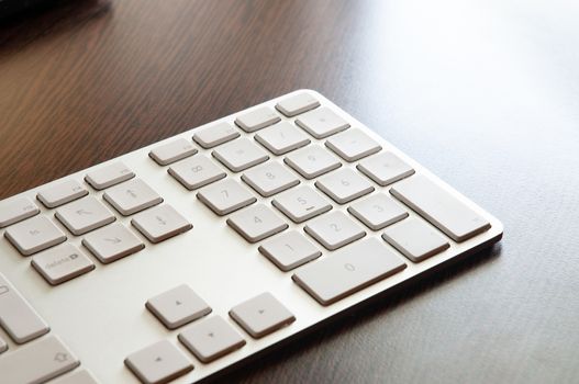 A light gray numeric keyboard on a dark wooden desk table