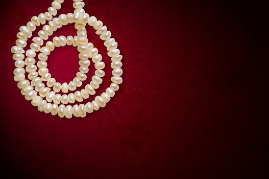 Natural pearls necklace in spiral on a red background, with space for copy text