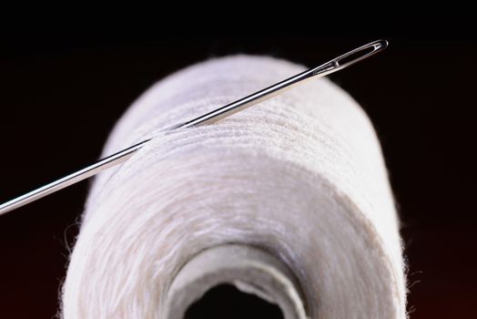 Macro of a white thread roll and needle  on black background