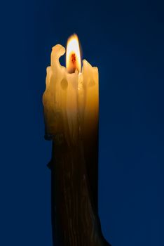 An old candle with a flame in the blue night