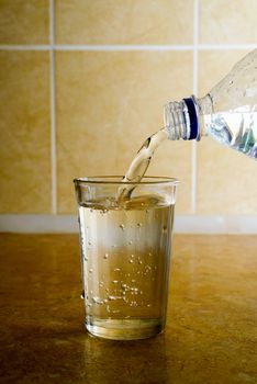 Pouring fresh mineral water from a plastic bottle into a simple glass in kitchen