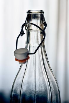 Detail of a glass bottle with a  wire bail clasp ceramic stopper in front of the window with white curtain