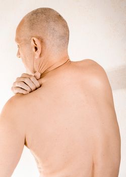 Man massaging his top back, the trapezius muscle, because of a thoracic vertebrae pain due to a displacement of a dorsal vertebra rubbing on a nerve