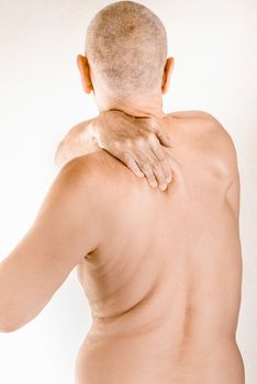 Man massaging his top back, the trapezius muscle, because of a thoracic vertebrae pain due to a displacement of a dorsal vertebra rubbing on a nerve