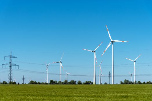 Overhead power lines and wind power plants under a blue sky in Germany