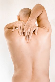 Man massaging his top back, between the shoulders, because of a thoracic vertebrae pain due to a displacement of a dorsal vertebra rubbing on a nerve