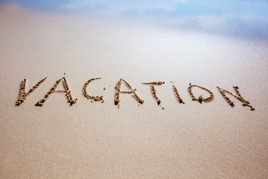 Word vacation written in a sandy tropical beach with soft sea wave