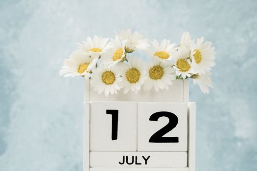 White cube calendar for july decorated with daisy flowers over blue background with copy space