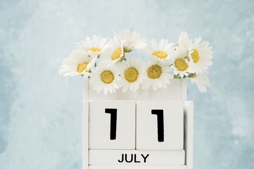 White cube calendar for july decorated with daisy flowers over blue background with copy space