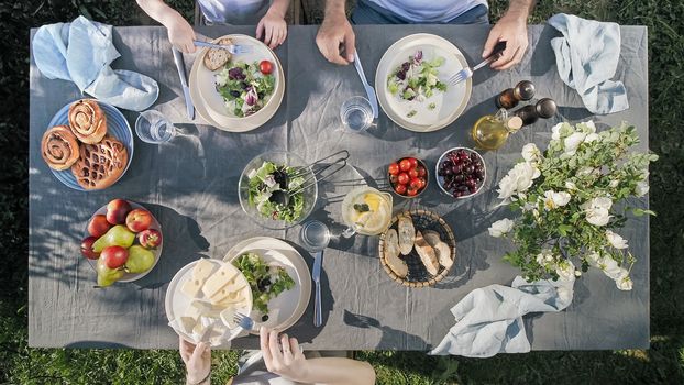 Family dinner outdoors. Family dinner with organic salad and cheese on trendy scandinavian style table in garden. Healthy aesthetic beautiful food, summer staycation concept. Aerial view or top view