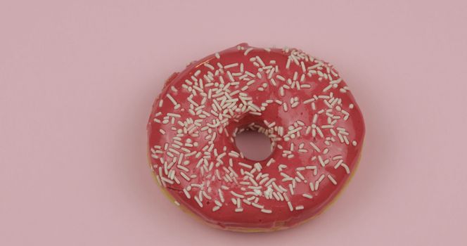 Delicious, tasty and fresh donut. Top view. Bright and colorful sprinkled sweet red donut close-up macro shot on a pink background