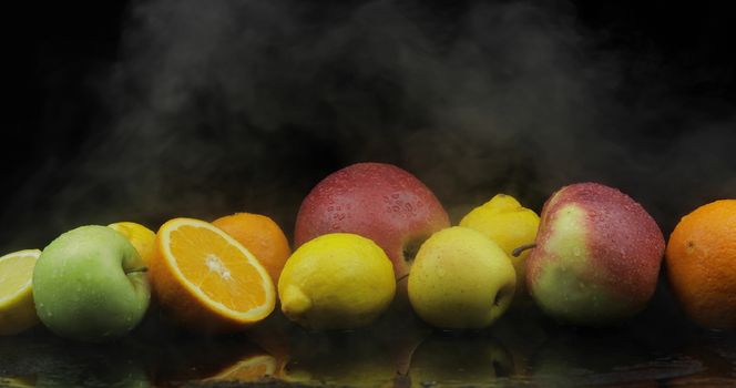 Tropical lemon, orange, apple in cold ice clouds of fog smoke on black background. Fresh and tasty fruits. Concept of healthy and rich in vitamins food