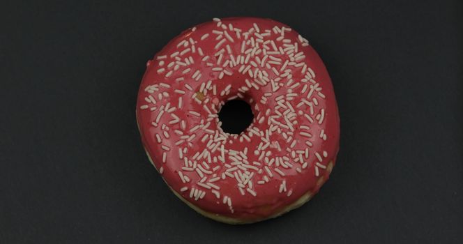 Delicious, tasty and fresh donut. Top view. Bright and colorful sprinkled sweet red donut close-up macro shot on a black background