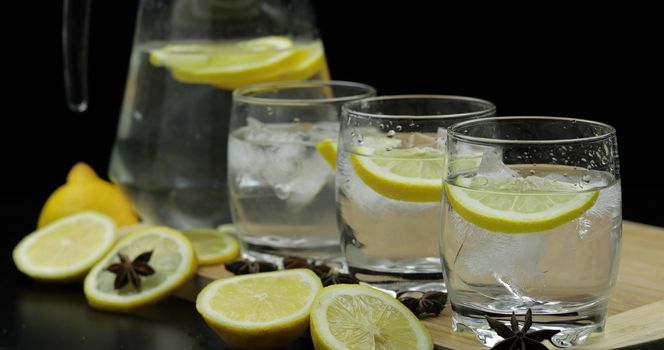 Lemon juice with ice and lemon slices in glass. Lemon cocktail with ice on dark background. Refreshing cocktail drink