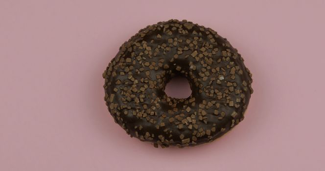 Delicious, tasty and fresh donut. Top view. Bright and colorful sprinkled sweet brown donut close-up macro shot on a pink background