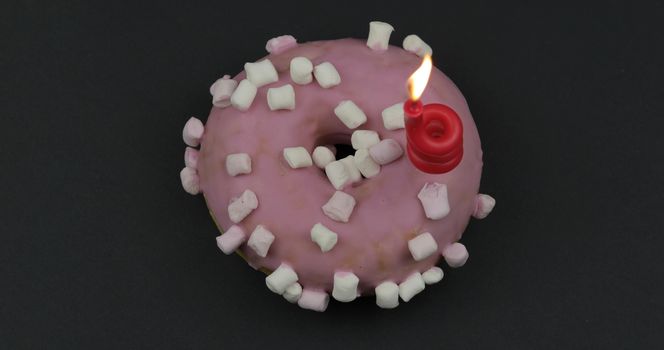 Delicious, tasty and fresh donut with festive candle. Top view. Bright and colorful sweet pink donut close-up macro shot on a black background