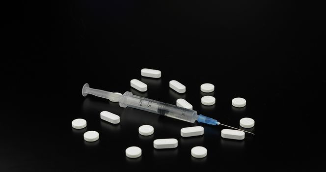 Pills and syringe with vaccination on black background.