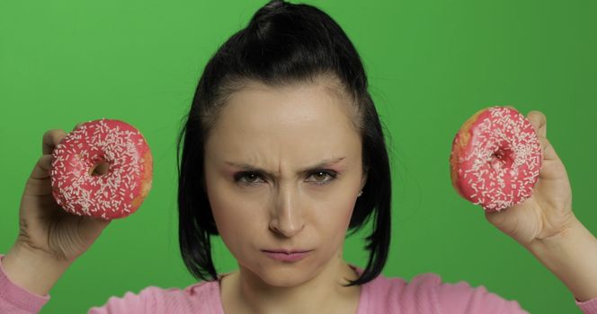 Happy beautiful young girl on a chroma key background having fun with donuts. Cute woman in a pink shirt posing with donuts. Making faces