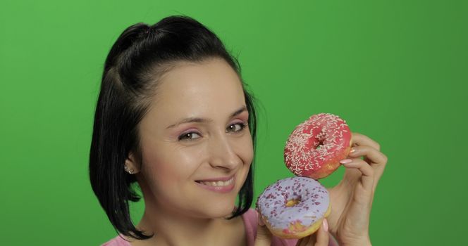 Happy beautiful young girl on a chroma key background having fun with donuts. Cute woman in a pink shirt posing with donuts. Making faces