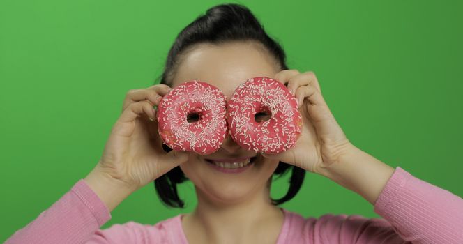 Happy beautiful young girl on a chroma key background having fun with donuts. Cute woman in a pink shirt posing with donuts. Making faces